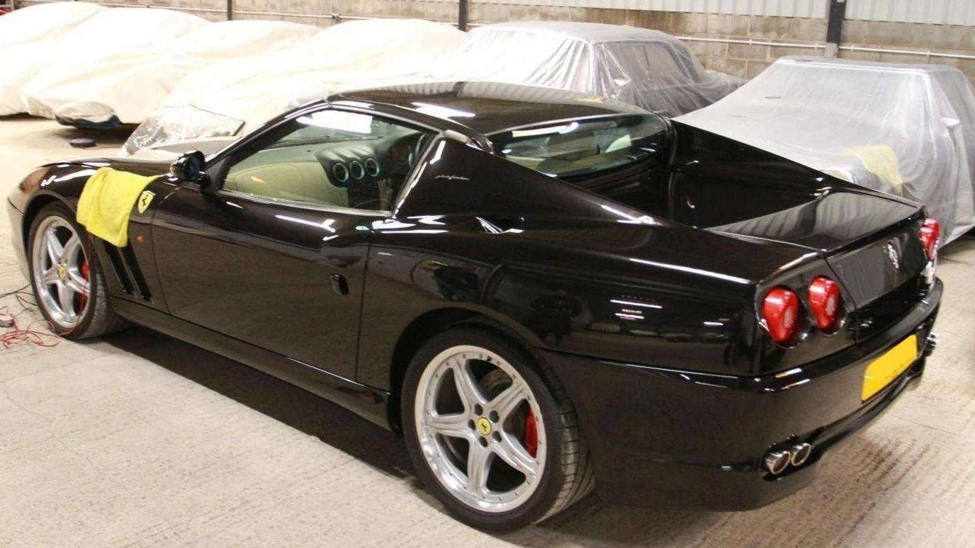 Image shows a black Ferrari Superamerica impounded in a warehouse