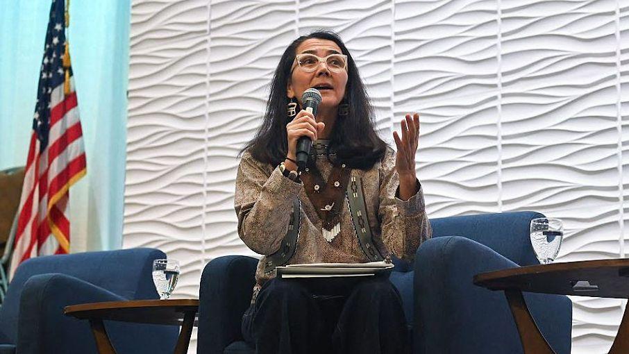 Mary Peltola holds a microphone and sits on a blue chair