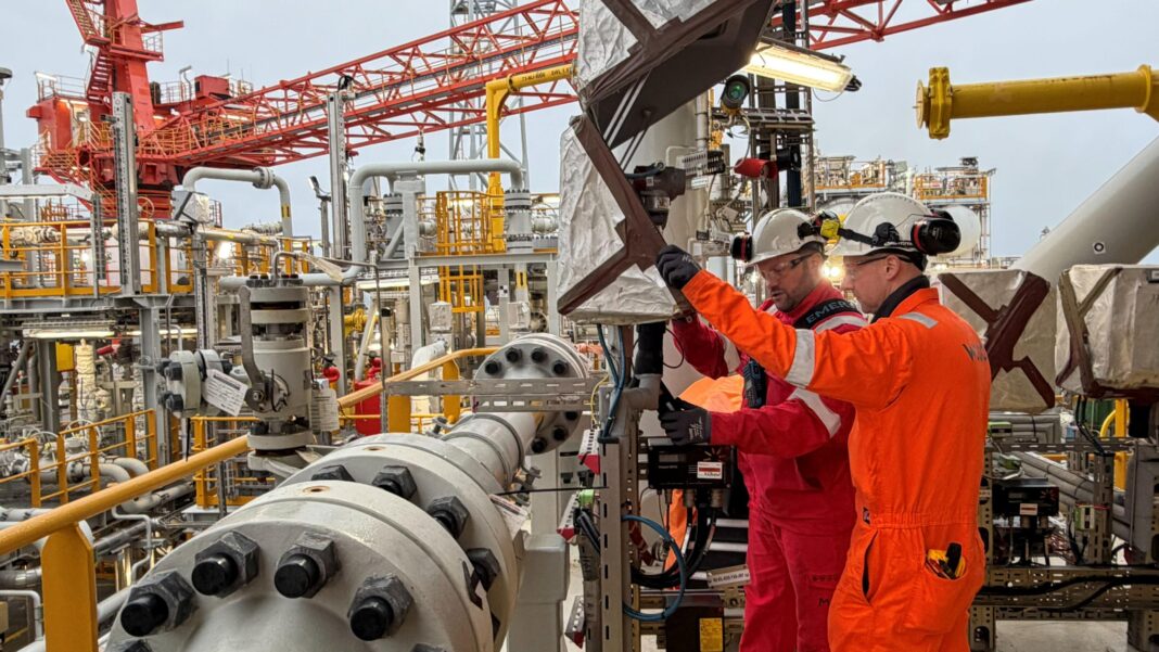 Workers wearing orange boiler suits examine equipment on board the Rosebank FPSO
