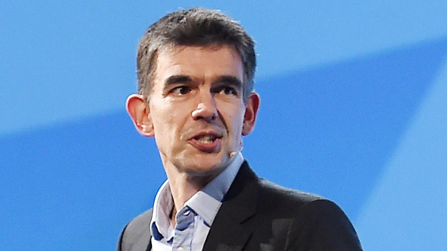 Matt Brittin looks at the audience while standing and speaking onstage against a blue background in London in 2016.