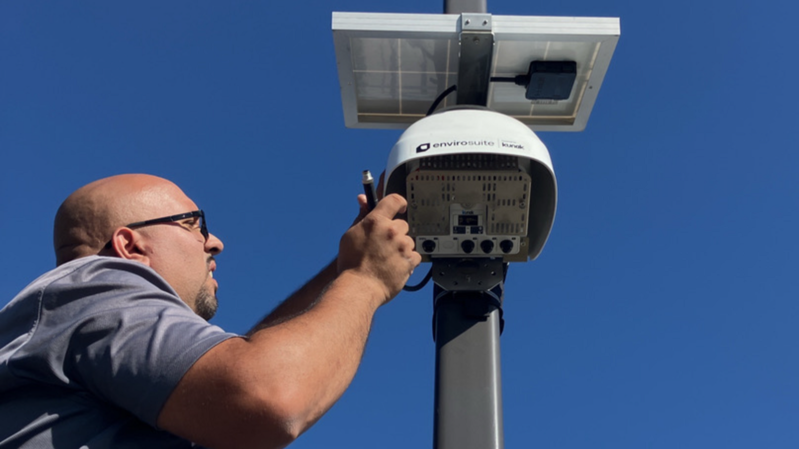 A technician in a t-shirt works on a Kunak monitoring which is attached to a pole.