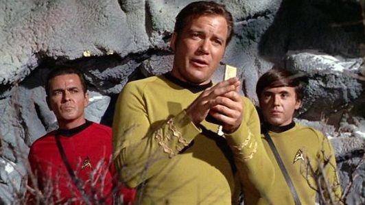William Shatner as Captain James T. Kirk speaking into his communicator with James Doohan as Montgomery "Scotty" Scott and Walter Koenig as Pavel Chekov (right) in an episode of Star Trek from 1968