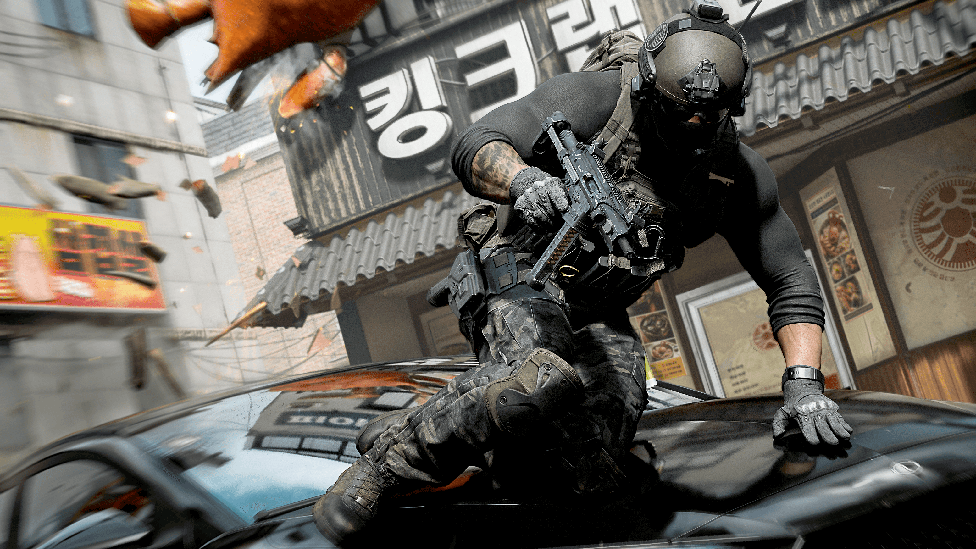 A still from Call of Duty Modern Warfare 4 showing a soldier leaping over a car on a South Korean street. He wears a helmet and protective gear and is armed with a large gun.