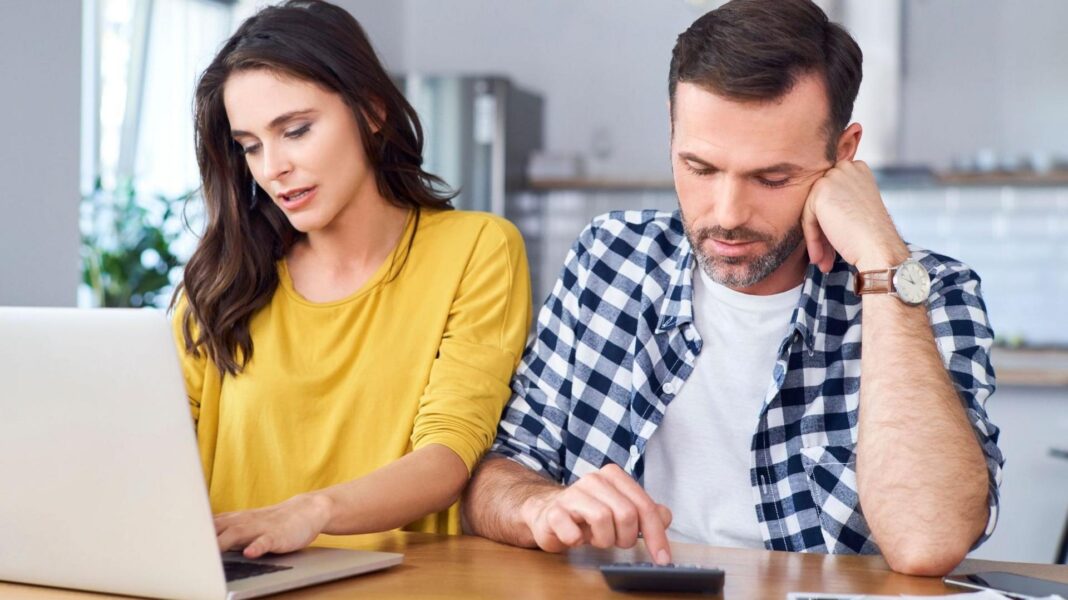 Home sellers cut asking prices on 3,000 properties a day Couple sit at a kitchen table with the woman in a yellow jumper looking at a laptop and the man in a blue and white shirt pressing numbers on a calculator.