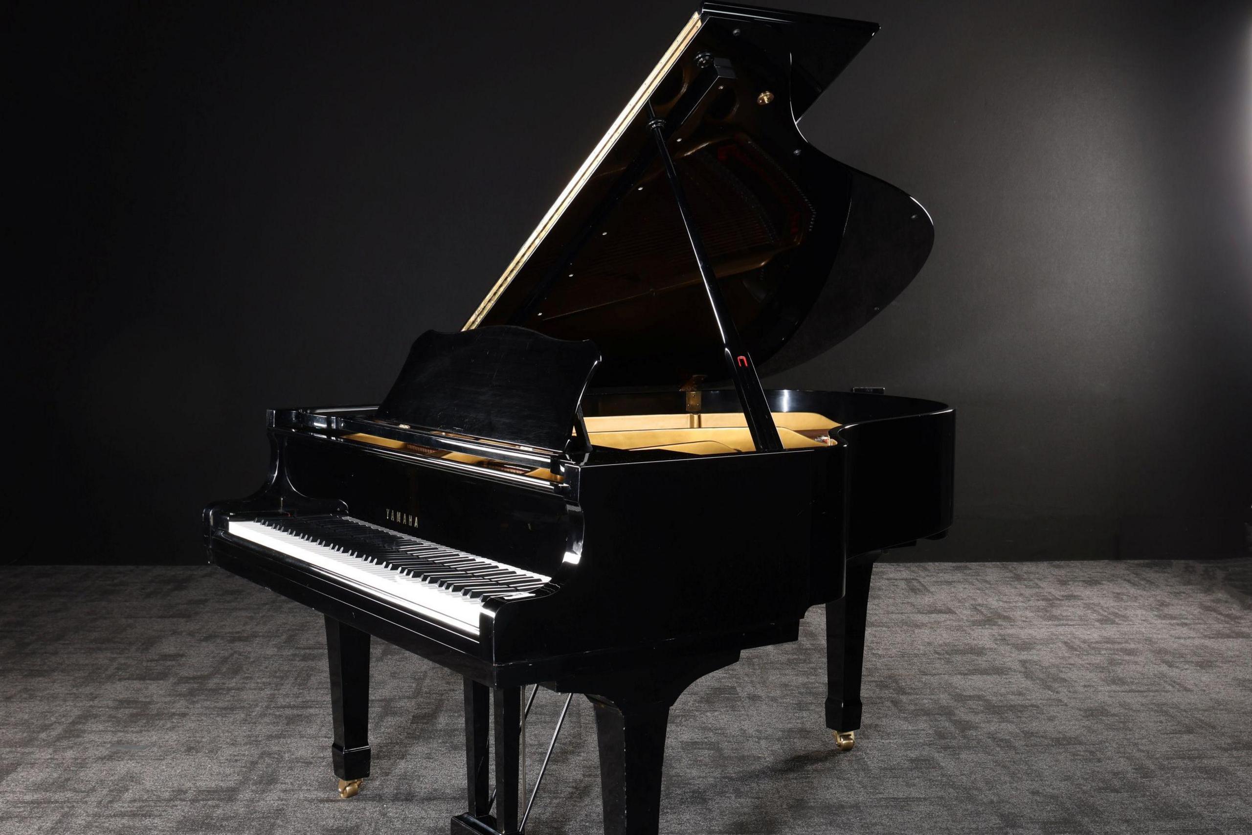 A black Yamaha grand piano standing in a dark room with grey carpet and black walls.