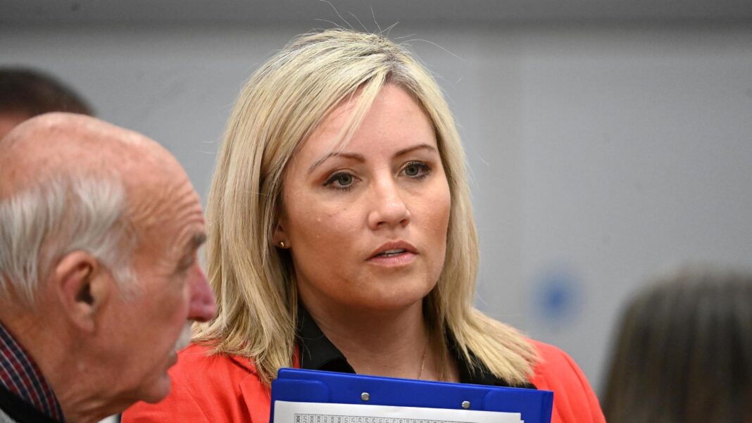 Diane Forsythe, who has long, blonde hair and holds a blue clipboard.