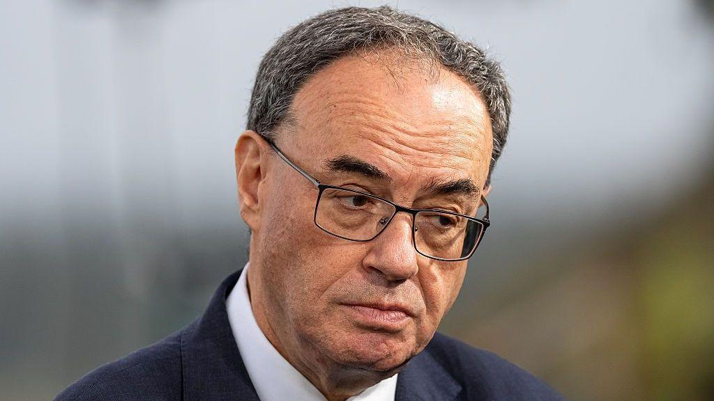 A close up of Bank of England Governor Andrew Bailey looking to one side wearing a navy suit and white shirt