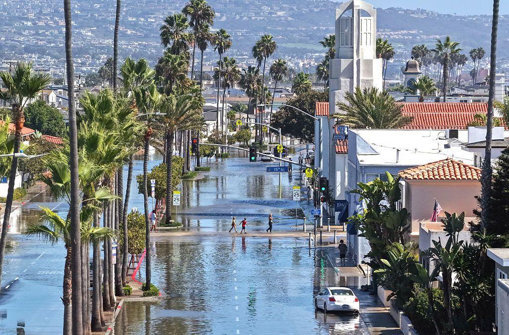 People walk near coastal floodwaters amid strong waves and high tides generated by Tropical Storm Rachel on October 9, 2026 in Newport Beach, California.