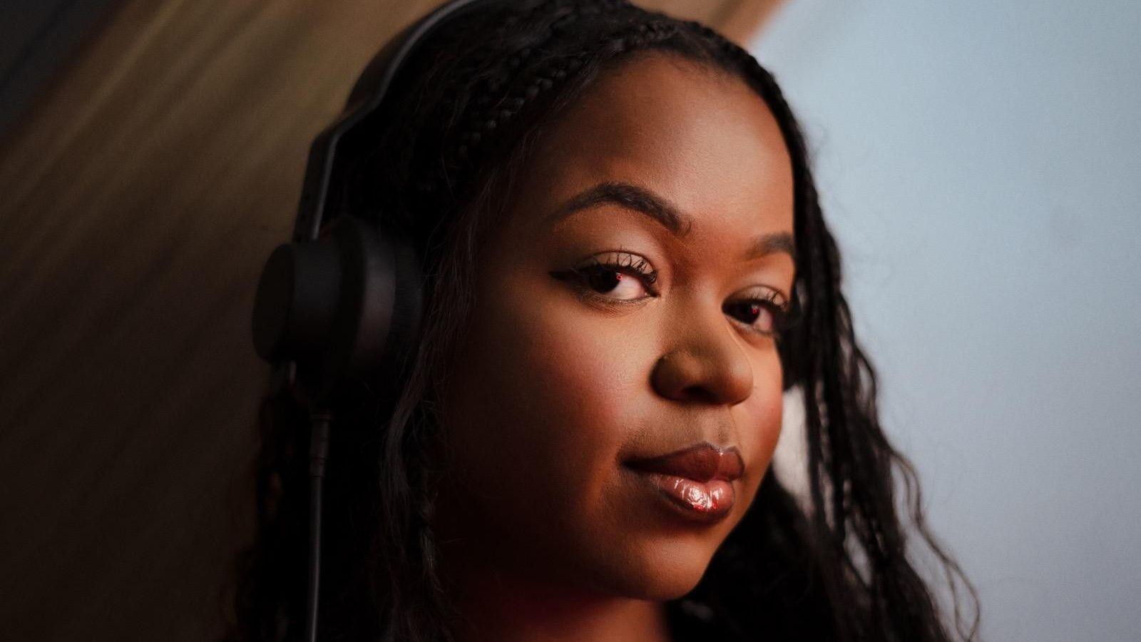 A professional headshot of Khaya Lou who has long dark-brown hair and is wearing headphones