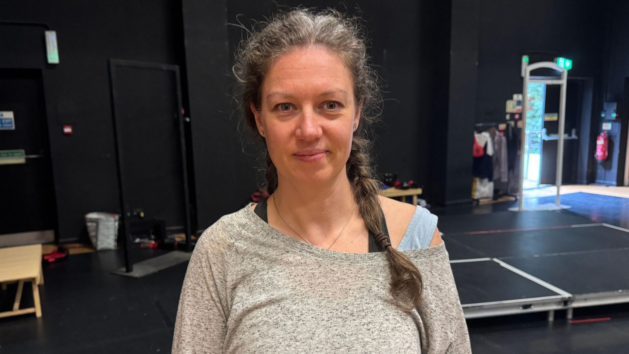 A lady wearing a grey long sleeved t-shirt. She is looking straight ahead.