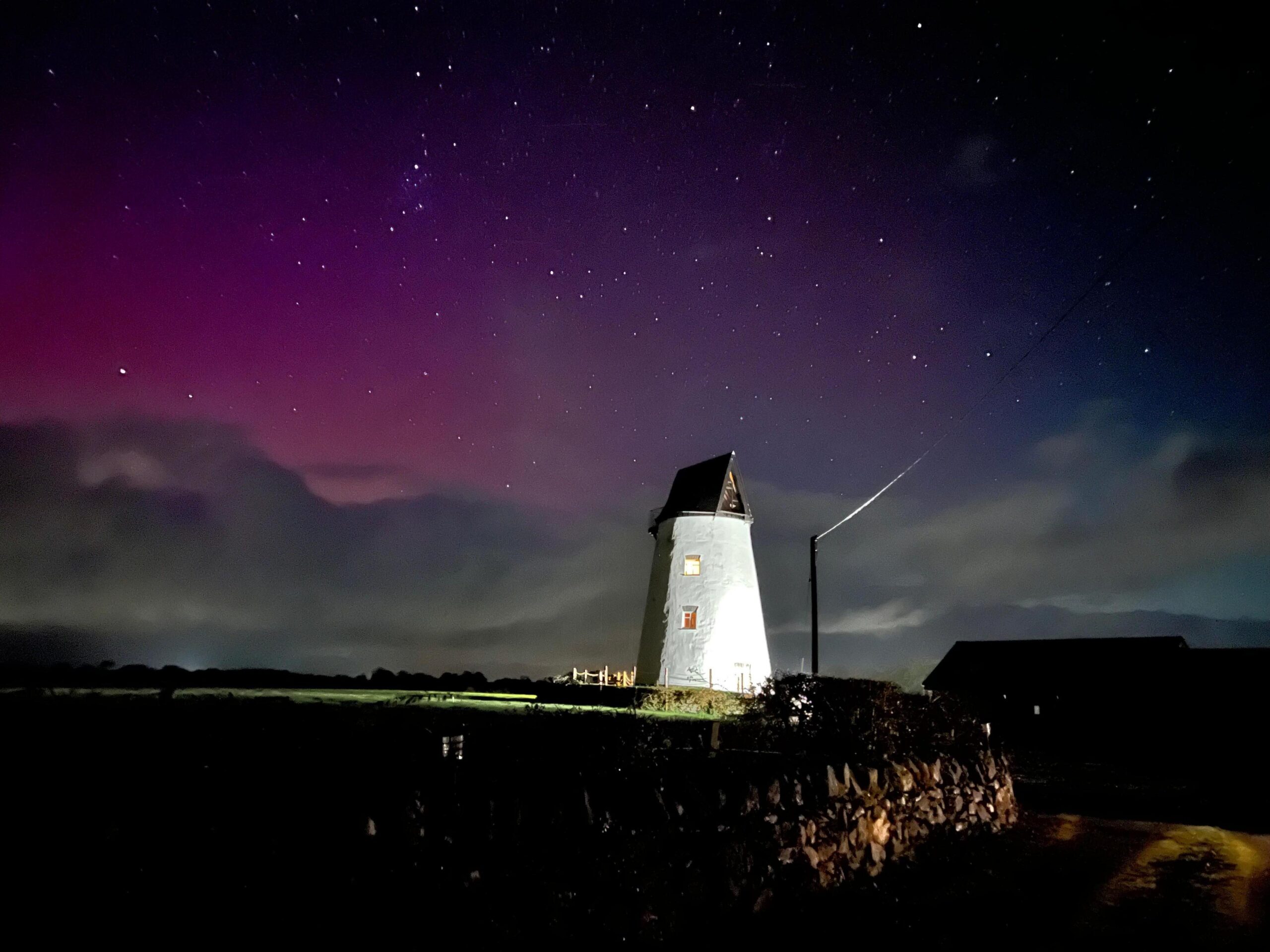An image of a star-filled sky and hues of pink and purple above a white-washed windmill-shaped building, on 10 October during the evening.