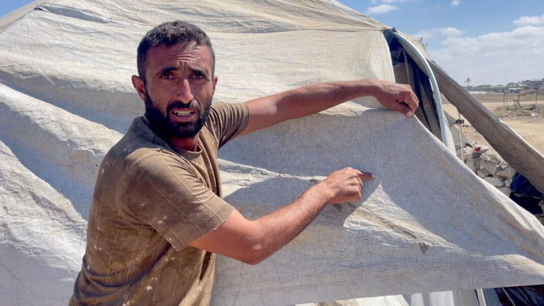 ‘Every day there is killing’: Gazans face Israeli strikes despite ceasefire as peace deal stalls A bearded man in a beige t-shirt points a piece of tent cloth he's holding up, in the Gaza Strip