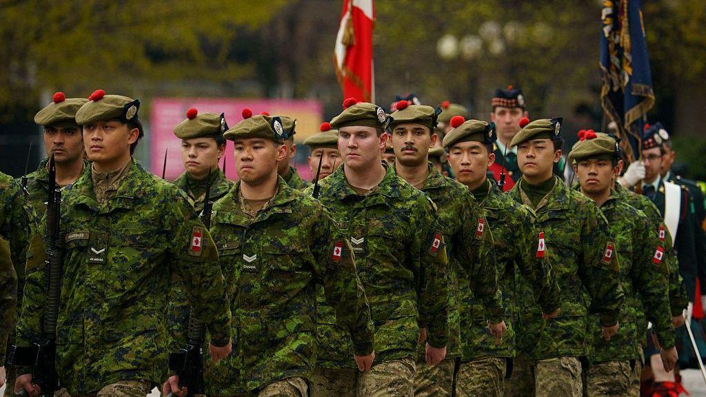 Canadian troops wearing green camouflage and wearing berets march