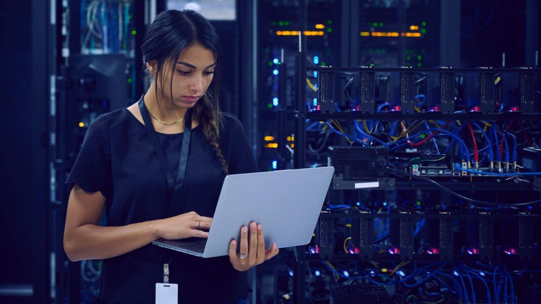 Trump’s green card curbs test Indian tech workers’ American dream A female technician dressed in navy blue clothes and wearing a lanyard around her neck is standing in a server room using her laptop.