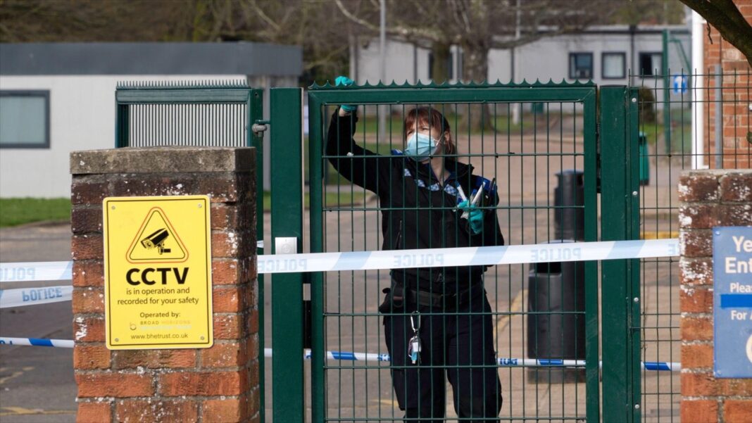 Teenage boy guilty of trying to murder girl, 15, in school A police officer wearing black uniform and turquoise gloves takes swabs from a green school gate, which is surrounded by blue and white police tape.