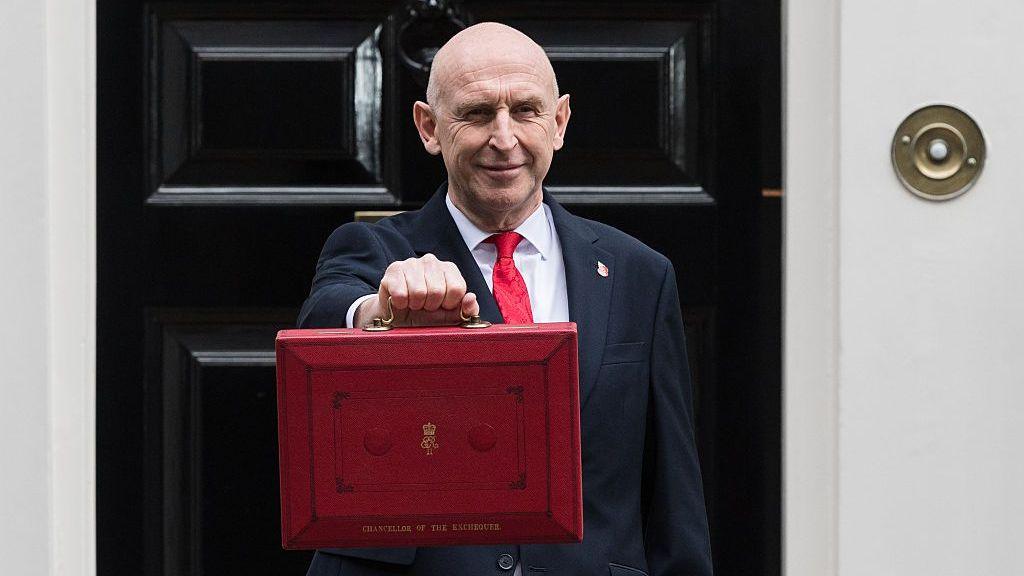 John Healy stands in front of Number 11 Downing Street while holding the signature red Budget box.