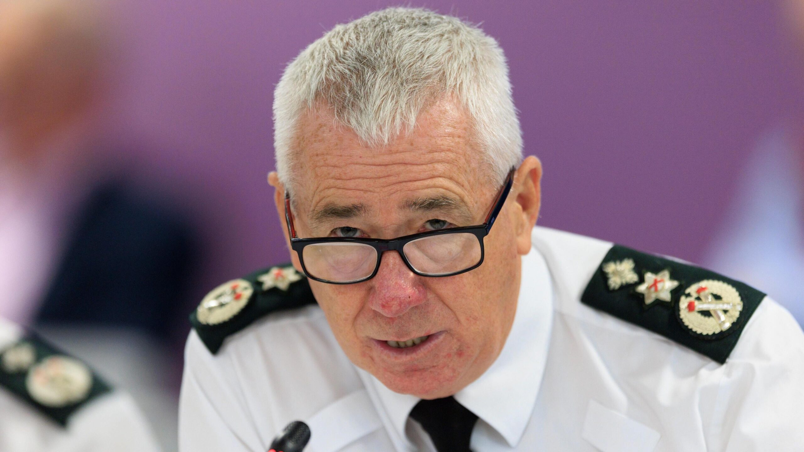 Jon Boutcher, with short grey hair, wearing a white shirt, black tie and glasses.