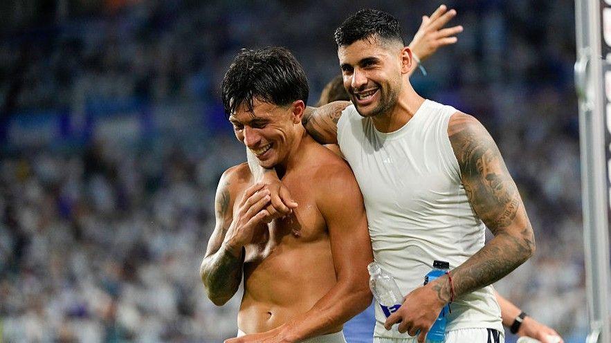 Argentina team-mates Lisandro Martinez, who is topless, and Cristian Romero, who is wearing a vest. Romero has an arm around Martinez as both smile