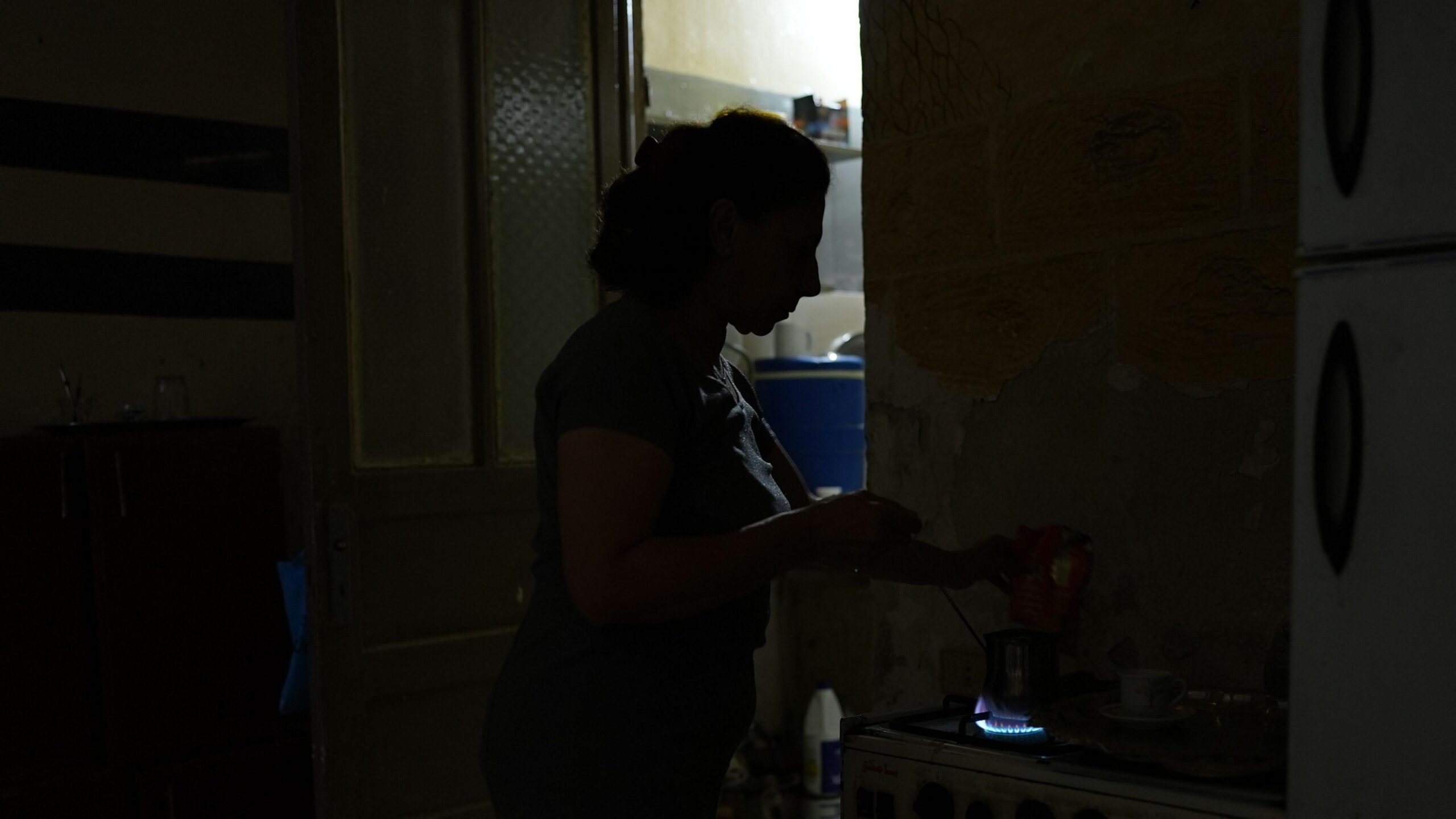 Profile of a woman heating up water on a stove standing in near darkness