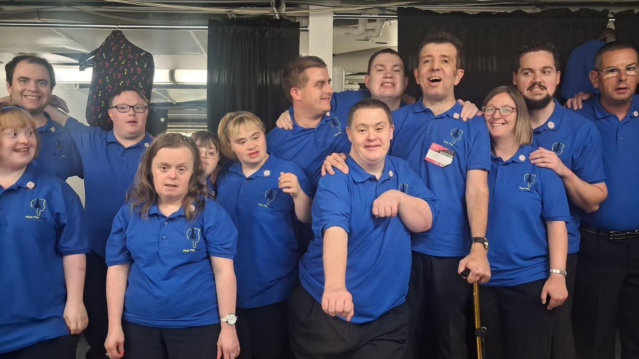 A group of performers with blue tops on posing for a picture backstage.