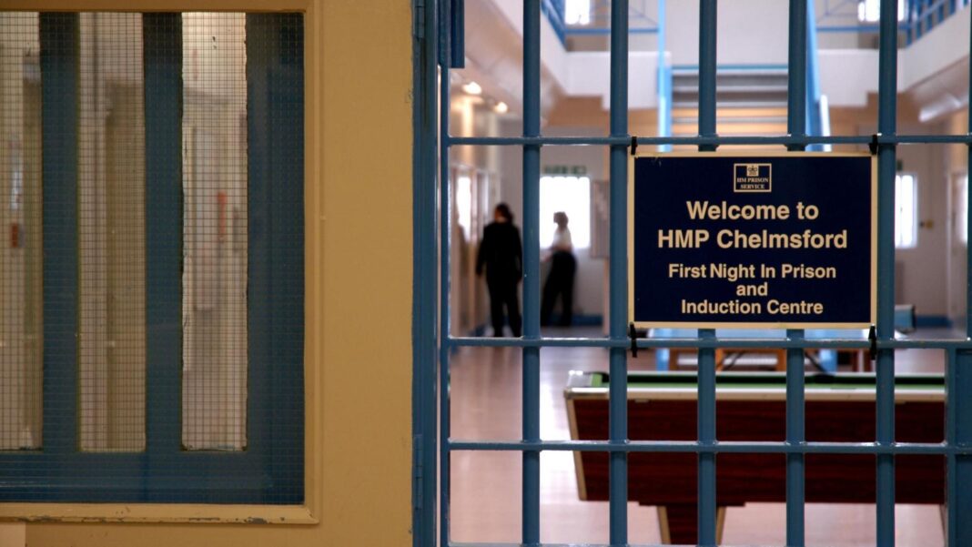 The inside of a prison has blue bars and a staircase in the background, with a large sign that says Welcome to HMP Chelmsford