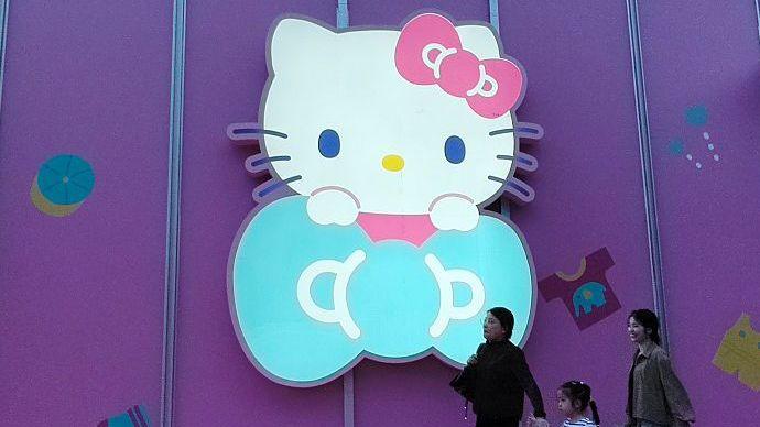Three women walk past a big glowing Hello Kitty signage on a purple store wall in Shanghai, China
