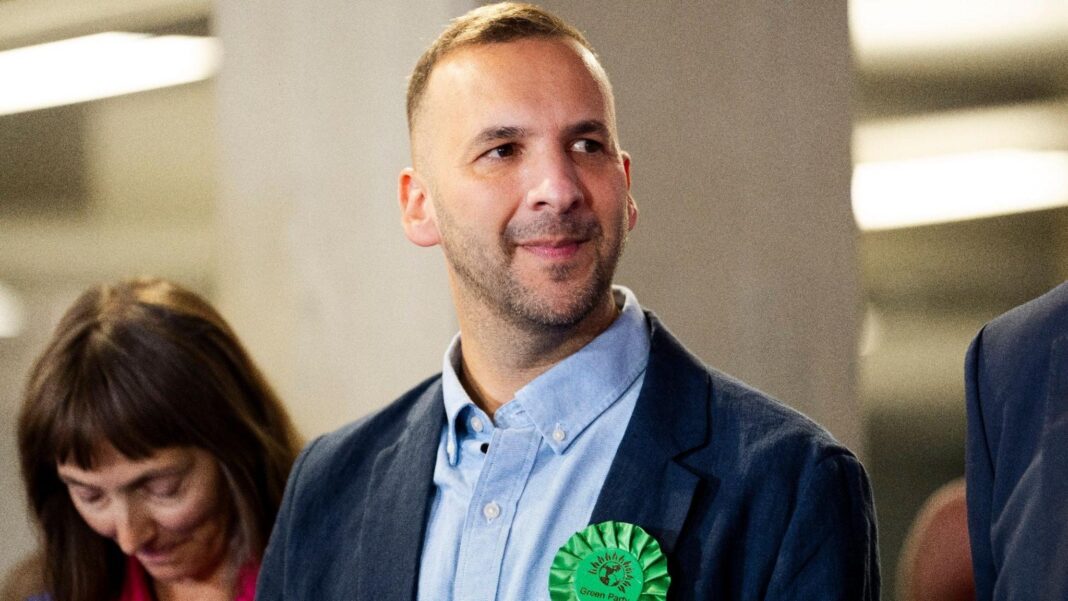Zack Polanski leader wearing a Green Party rosette at the by-election count