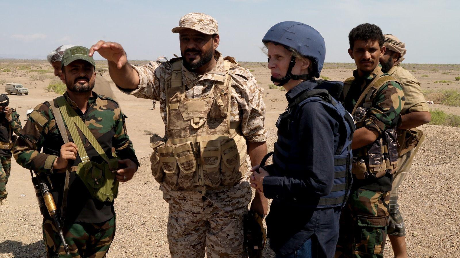 Commander Tawfiq Al Haboun in combat fatigues gestures next to Orla Guerin wearing blue in a group of armed people wearing combat fatigues
