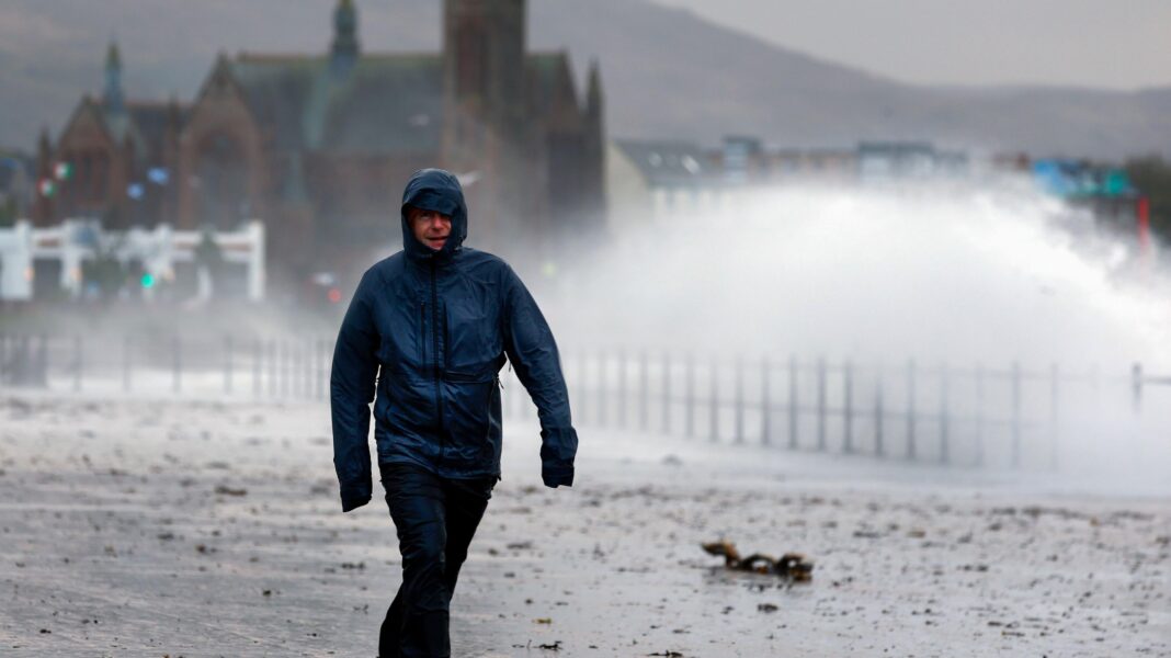 Wettest week for two years but still not enough rain to get out of drought Man walking along a coastal promenade with waves and sea spray crashing onshore. The man is looking very wet