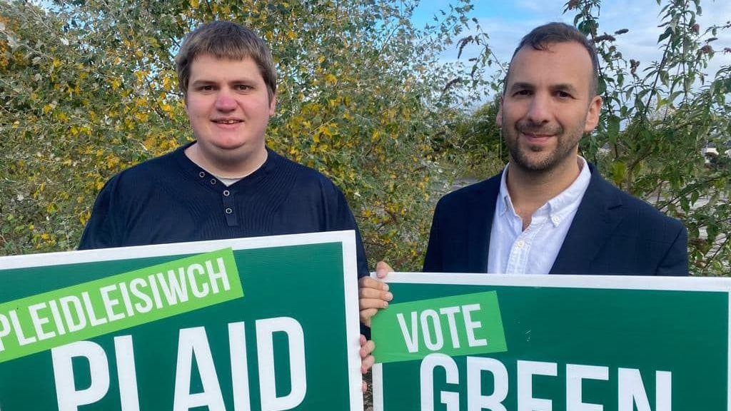 Phil Davies, a man with brown hair, holds a vote Green Party sign translated into Welsh. On the right, party leader Zack Polanski wearing a suit holding a sign encouraging people to vote for the Green Party.