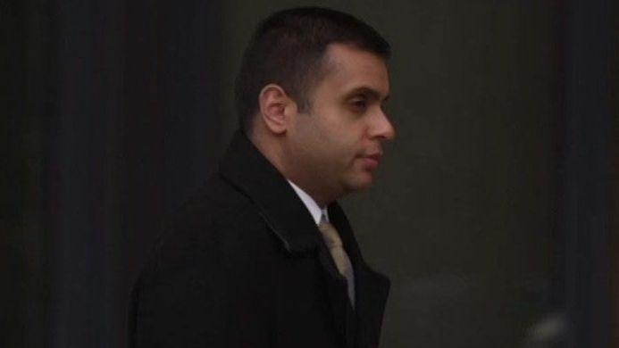 Faisal Shoukat pictured walking away from the court wearing a black overcoat and gold tie. He is carrying a briefcase.