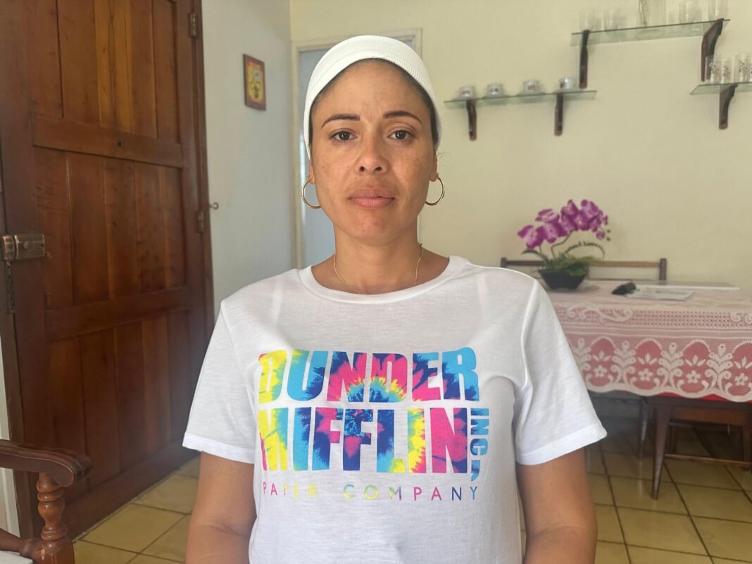 Heydi Sanchez looks at the camera while standing in her kitchen, wearing a brightly coloured t-shirt