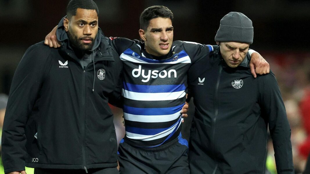 Pepper to miss England games and Carreras’ season over Santi Carreras in blue, white and black Bath shirt with arms round support staff as he is helped off the field