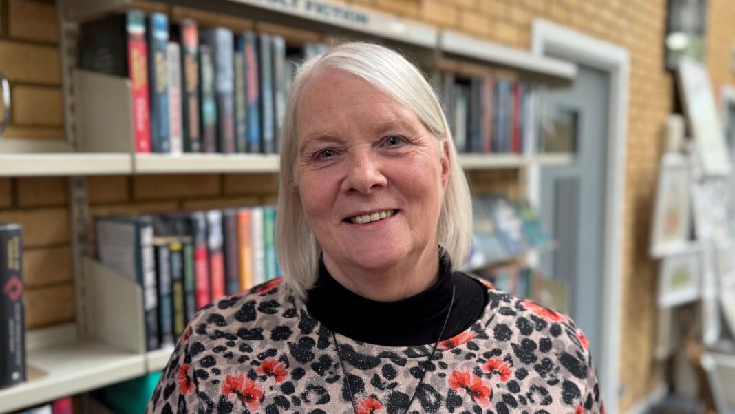 What books had people turning pages and turning up the volume this year? Women with short white hair, standing in front of a bookshelf wearing a black and grey top with red flowers on it.