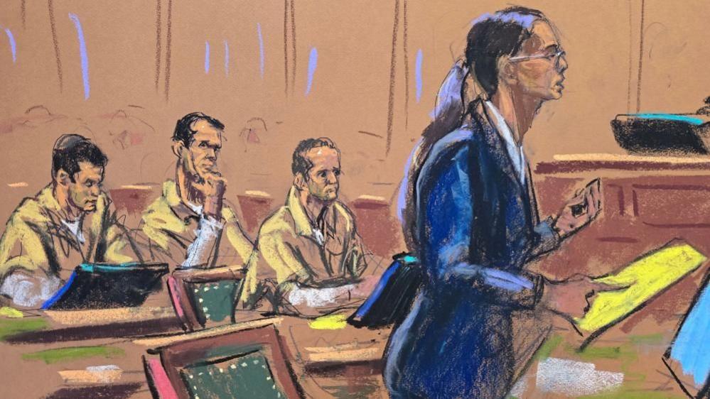 A court sketch of a woman in a blue suit with glasses and long brown hair tied back in a ponytail addressing a courtroom while three men in khaki prison jumpsuits sit watching.