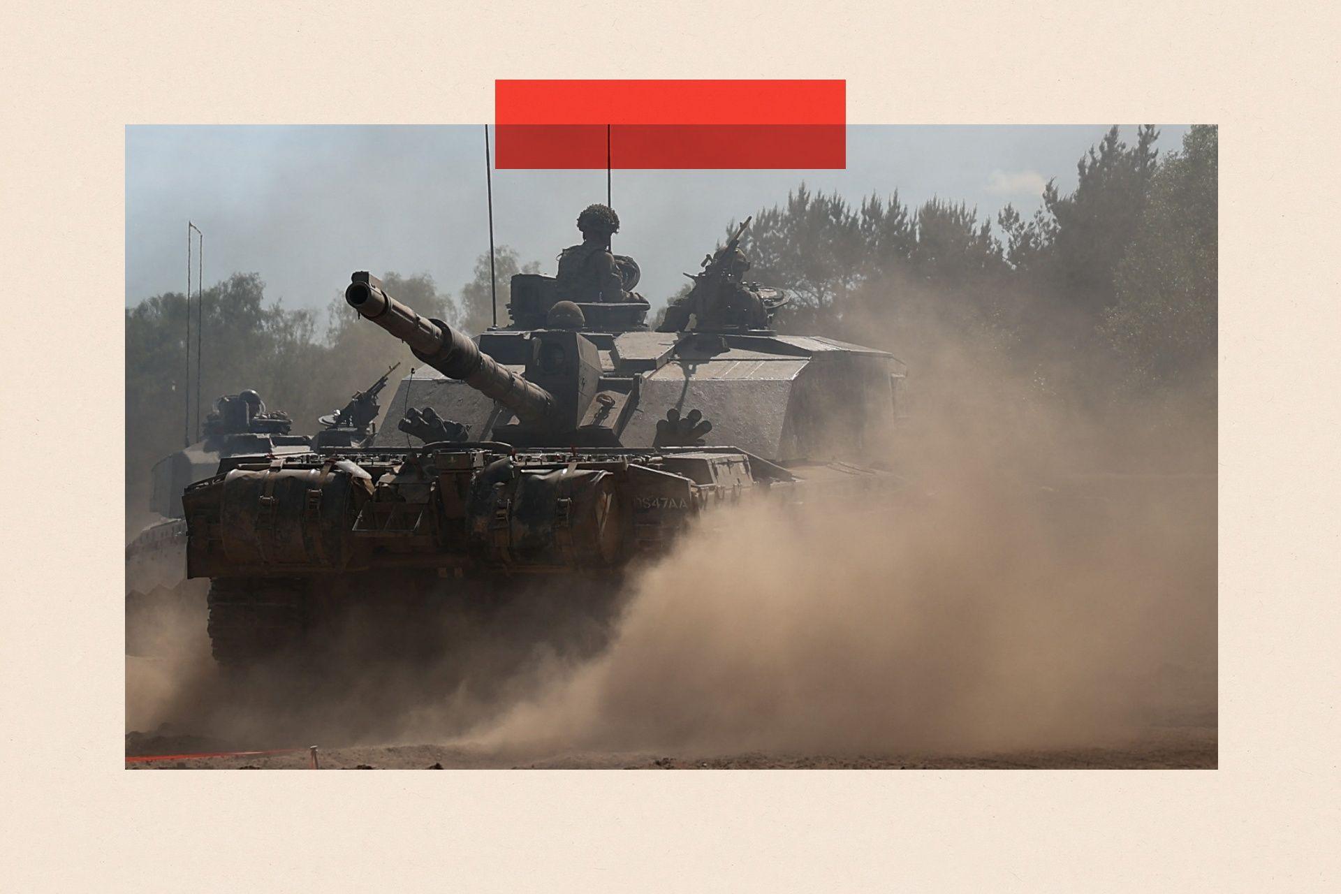 A tank on a dusty road with soldiers wearing helmets and military clothing seen riding the tank.