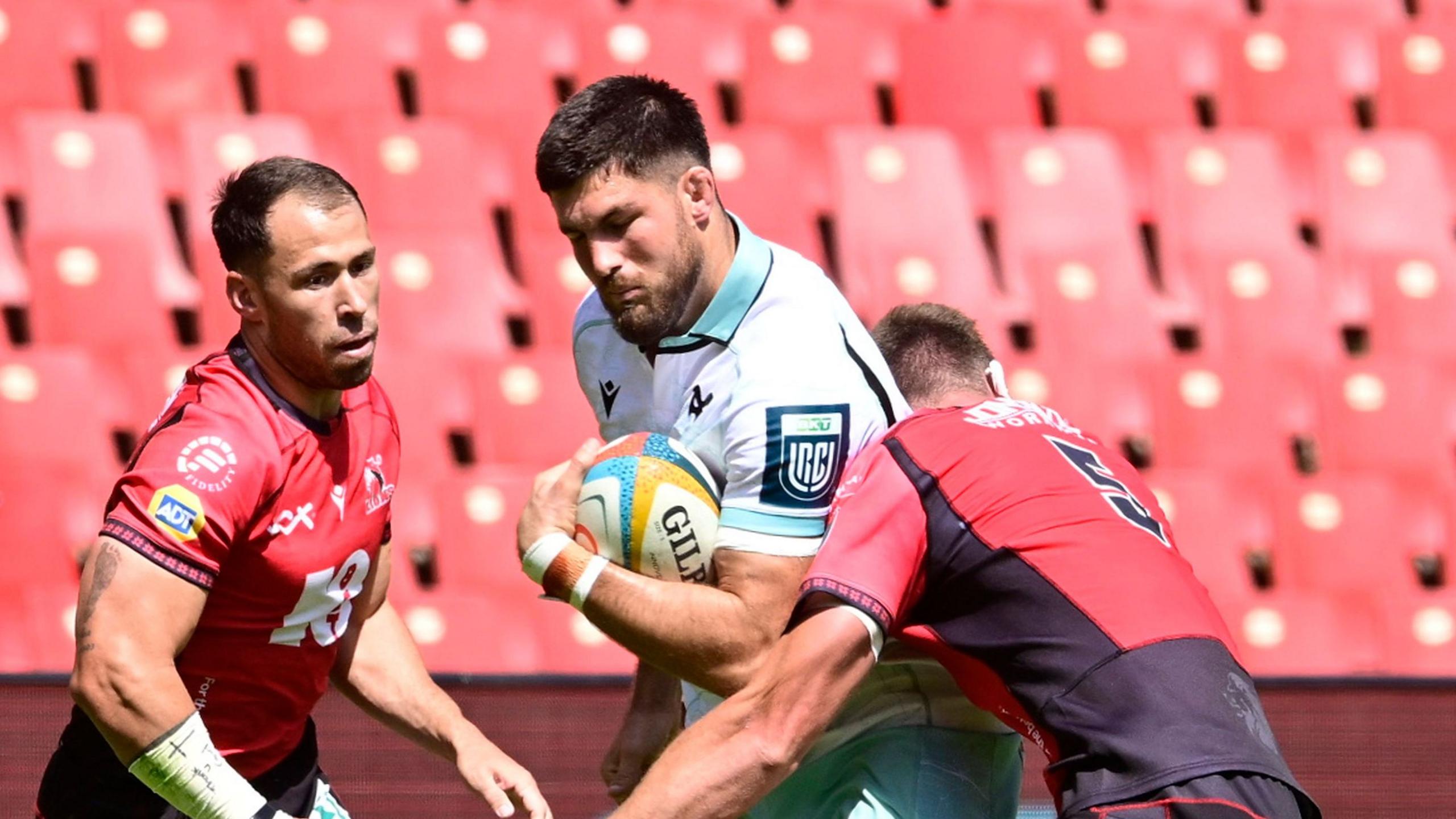Liam Wright in white carries the ball for Ospreys challenged by two red-shirted Lions players