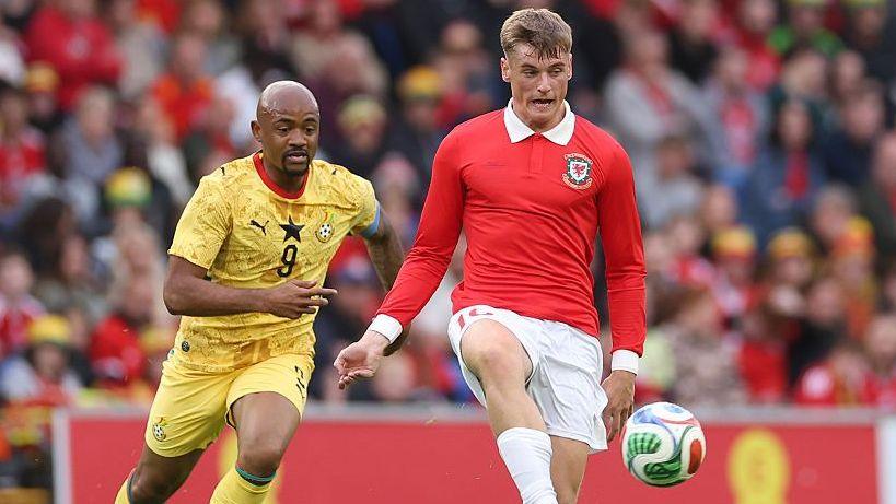 Dylan Lawlor in the red shirt of Wales controls the ball under challenge from an opponent in yellow