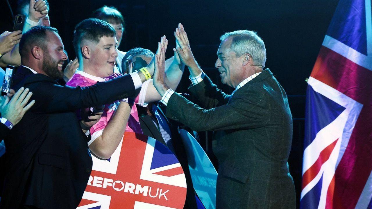 Reform leader Nigel Farage on the right greeting supporters at the rally in Plymouth with a Union flag in the background to the right