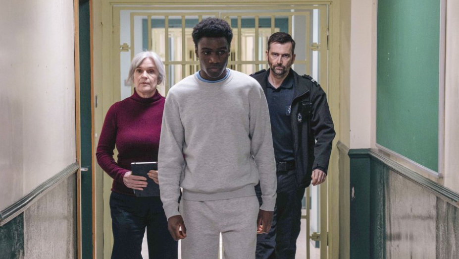 Still taken from the programme showing David Tennant and Siobhan Finneran walking along a corridor with a young boy who is wearing a grey tracksuit.