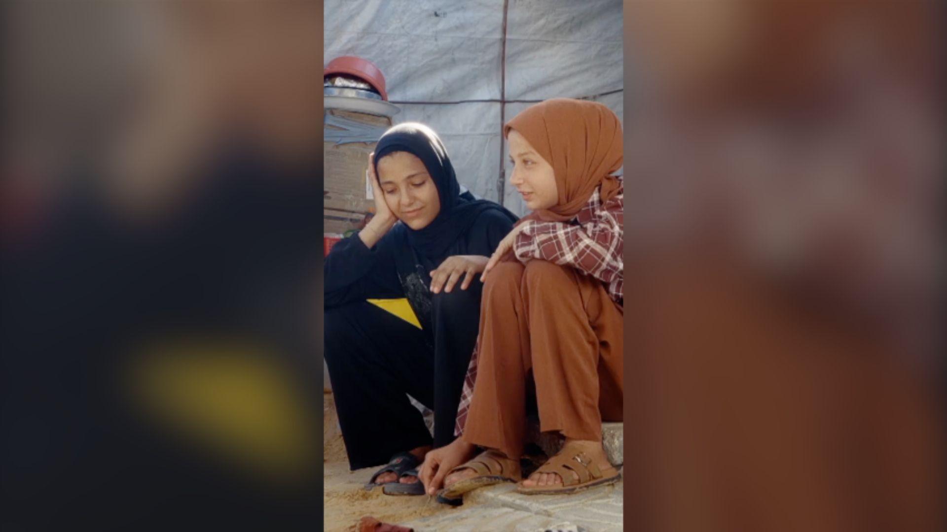 Two young girls sat on a step. One (left) is dressed in all black, the other (right) is dressed in light brown.