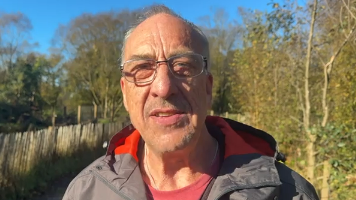 Chris Roberts has short hair and is wearing glasses. He is wearing a black and red coat.