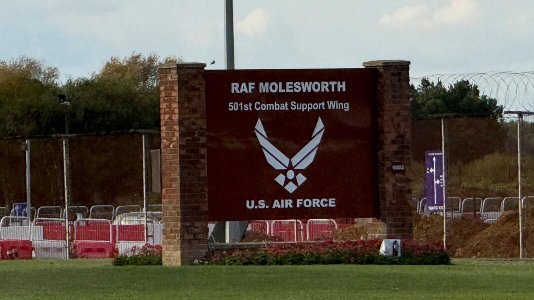 A large brown sign, fixed to brick posts, reads RAF MOLESWORTH and is at the entrance to a military base.