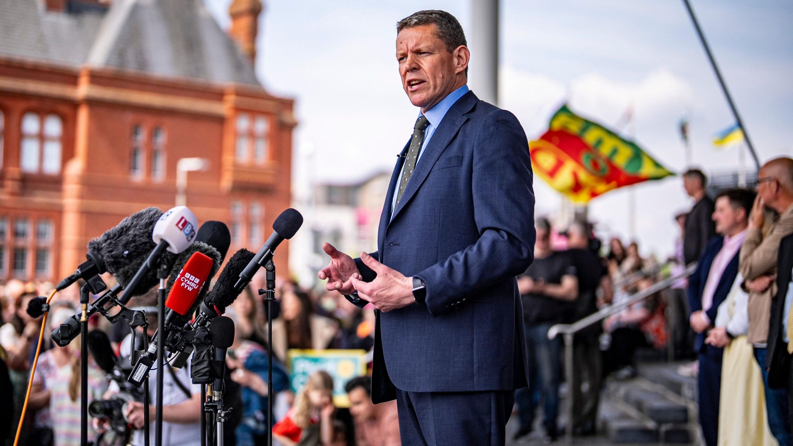 The image shows Rhun ap Iorwerth addressing a crowd outside the Senedd following May's Senedd election result.