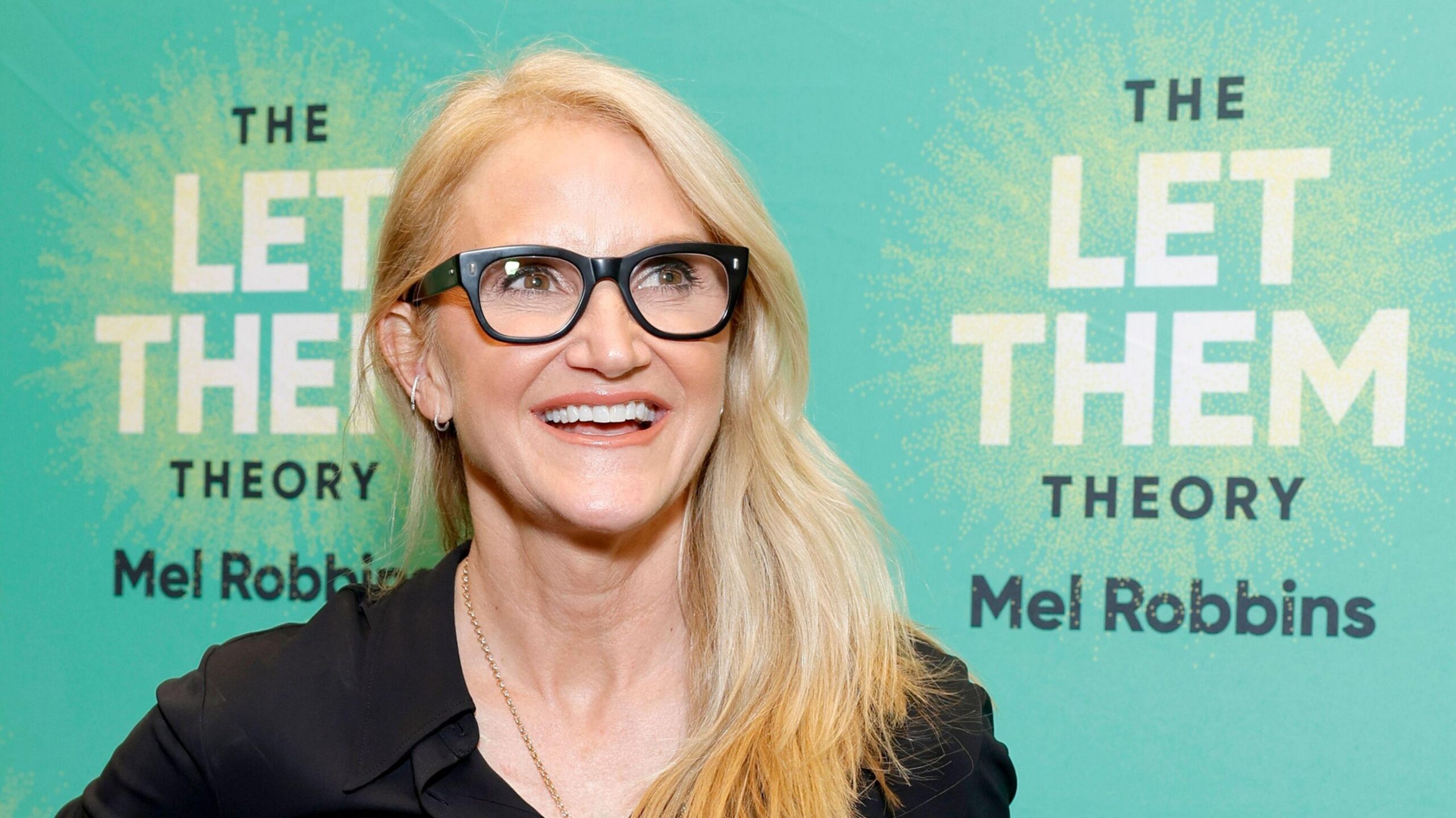Mel Robbins with long blonde hair wearing a black shirt and glasses. She stands in front of a green background which says 'The Let Them Theory Mel Robbins.'