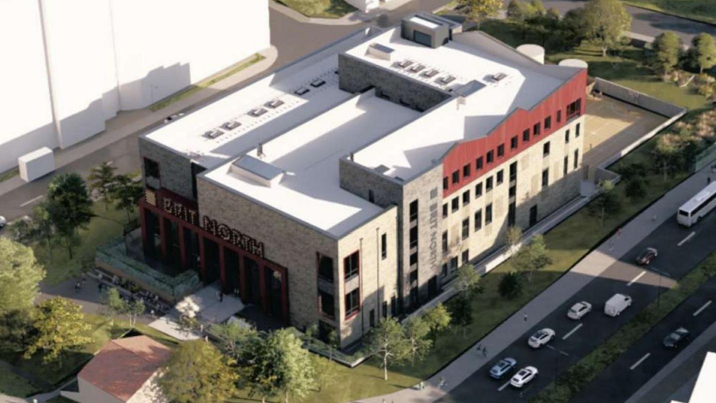 An aerial view of Brit North - a grey, brown and black stone building with a white roof. Around the large rectangular building are green patches and roads