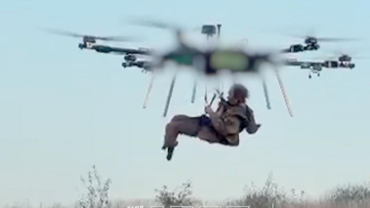 A man can be seen being flown while being carried by a drone