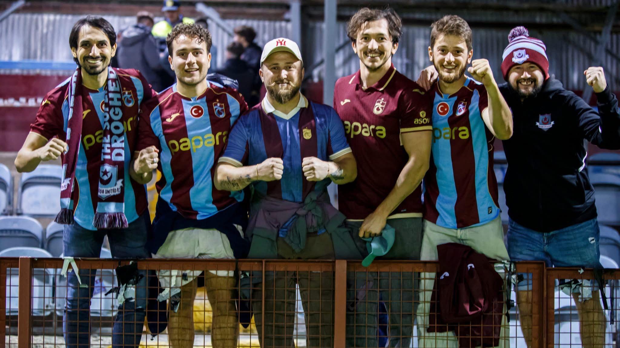 A group of Trabzonspor fans pose for the camera pitch-side at Drogheda's stadium.