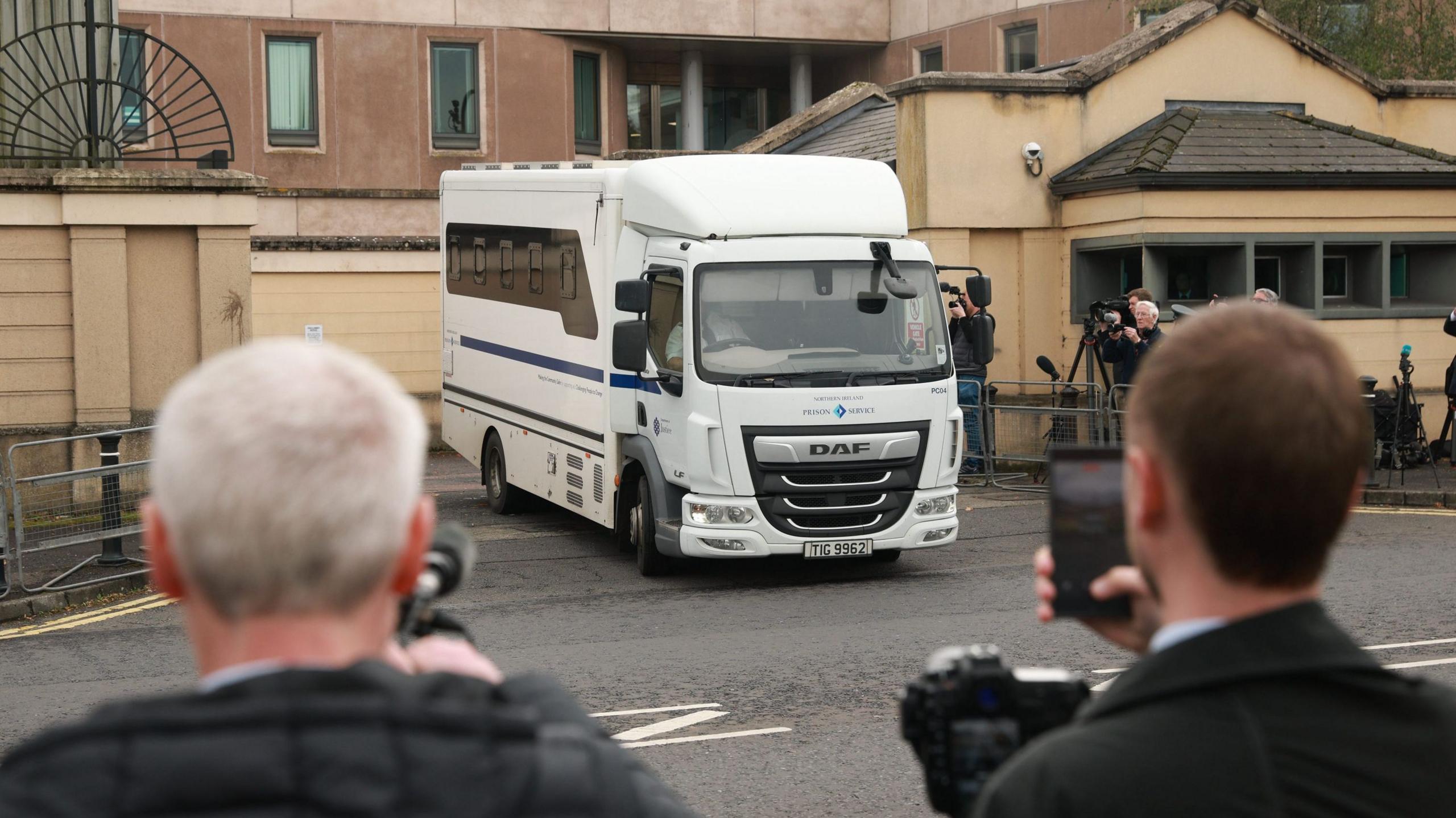 A white prison van carrying Jeffrey Donaldson travels past camera crews outside Newry courthouse.