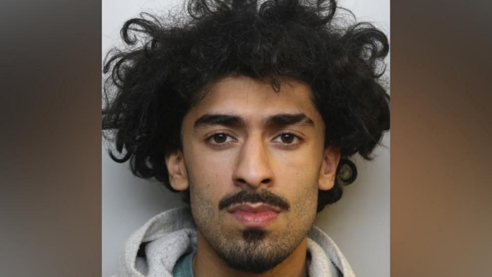 Police mugshot of Suleman Aqeel who is young man with facial hair and dark, curly hair.